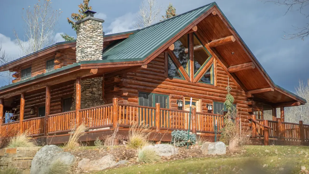 Swiss Chalet exterior with stone chimney and green metal roof, Meadowlark Log Homes