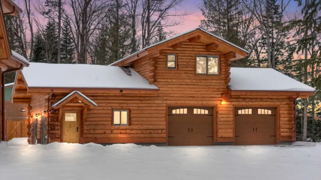 Rustic log home garage with snow in a forested winter landscape