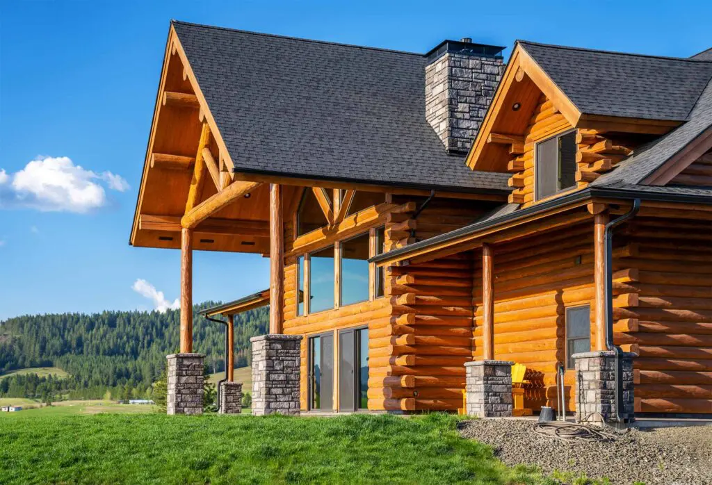 Beautiful exterior of log home with green grass and mountains in Montana